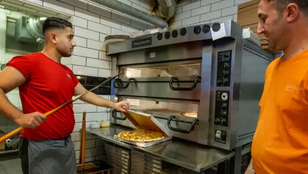 Två pizzabagare jobbar vid en stor pizzaugn. En tar ut en färdig pizza i Sverige.