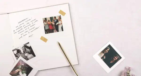Vœux de mariage manuscrits sur un album, avec des photos instantanées de la cérémonie et du couple. Un stylo doré repose à côté.