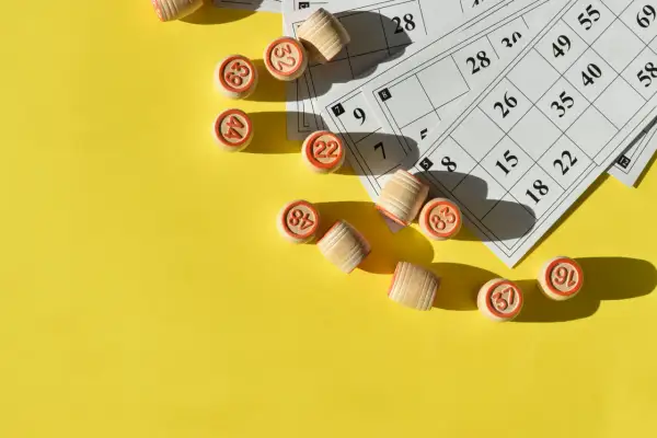 Drewniane krążki z numerami i karty do gry w bingo leżą na żółtym tle, gotowe do emocjonujących konkursów i loterii.