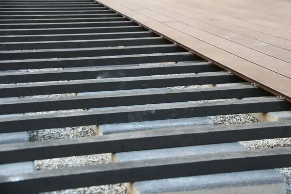Unterkonstruktion für eine WPC-Terrasse mit grauen Betonsteinen und dunklen Balken, bereit für die Verlegung der braunen Dielen.