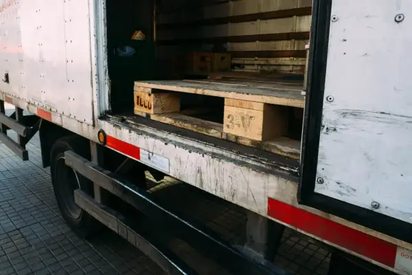 Wnętrze ciężarówki z widocznymi drewnianymi paletami, gotowymi do załadunku. Na jednej z palet widoczny napis "TCLU".