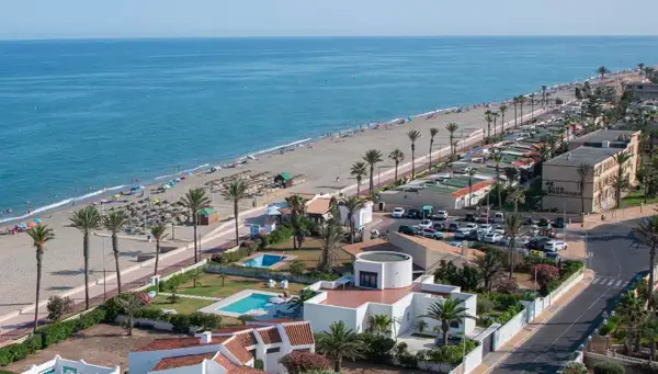 Vista aérea de la playa de las salinas, con gente disfrutando del sol y el mar, palmeras y edificios turísticos.