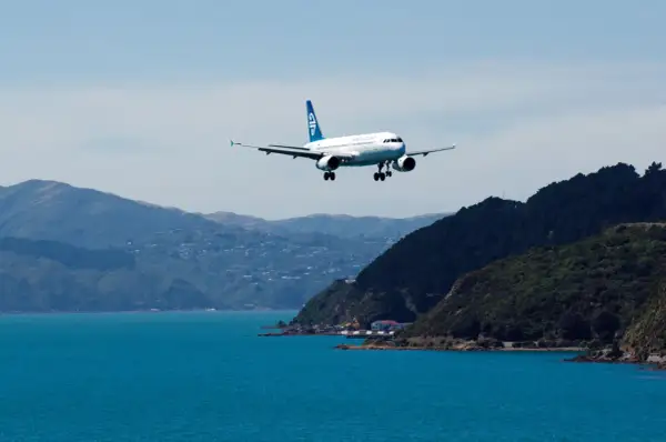 Samolot Air New Zealand ląduje nad turkusową wodą, zbliżając się do wybrzeża. Zastanawiasz się, ile kosztuje lot do Nowej Zelandii?