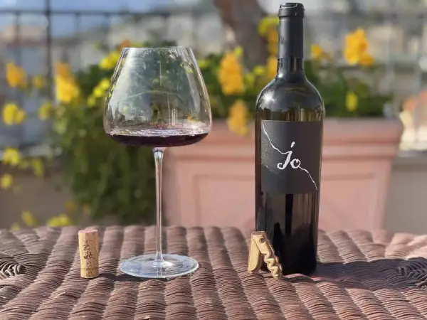 Un calice di vino rosso e una bottiglia di Negroamaro Puglia, con tappo e cavatappi, su un tavolo all'aperto.