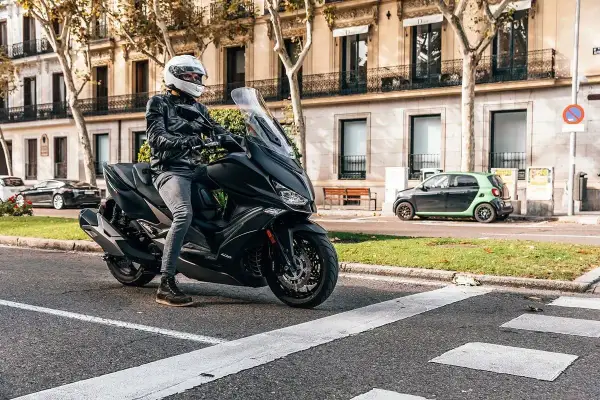 Conductor con casco blanco en un scooter negro, listo para rodar. Una imagen que evoca las mejores marcas de motos y la libertad en la ciudad.