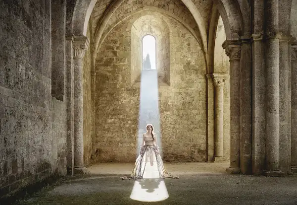 Cristina Vatielli, vestita di bianco, in piedi sotto un raggio di luce in un'antica abbazia.