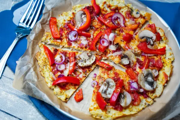 Vegane blumenkohl pizza mit Paprika, Zwiebeln und Pilzen, auf Backpapier serviert.