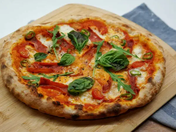 Pizza maison avec une pâte à pizza préparée la veille, garnie de tomates, mozzarella, roquette, basilic, piments et salami.
