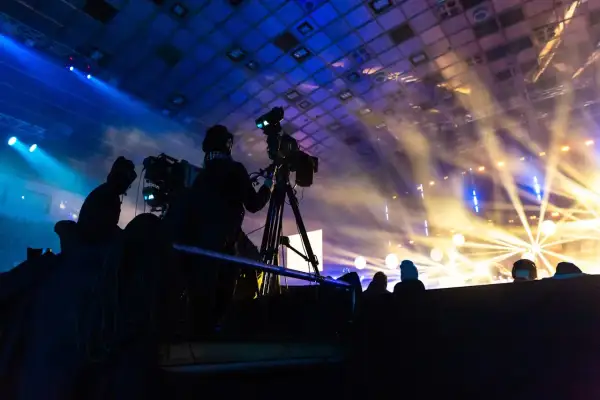 Operatorzy kamer w akcji podczas koncertu. W tle scena oświetlona reflektorami, tworząca magiczną atmosferę.