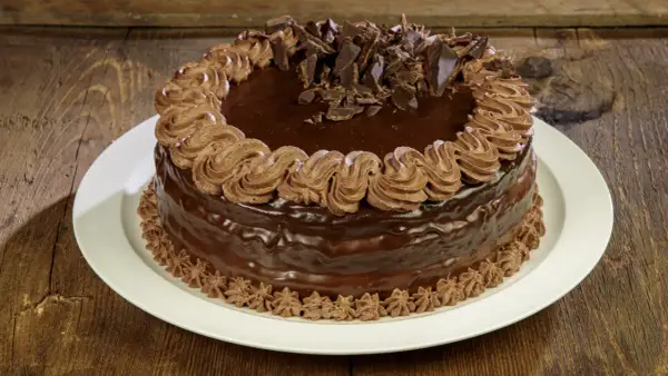 Torta compleanno cioccolato e panna, ricoperta di glassa lucida e decorata con riccioli di panna e scaglie di cioccolato.
