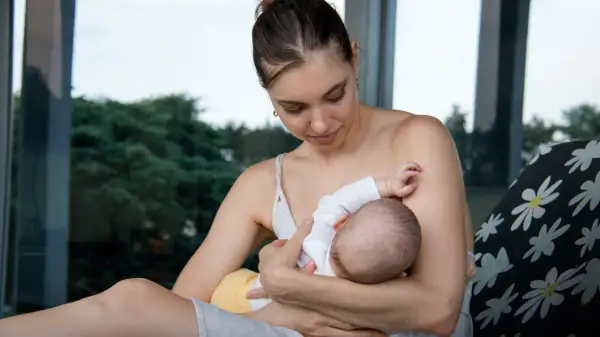 Delikatny moment karmienia piersią. Mama z miłością patrzy na swoje dziecko, które pije mleko z piersi.