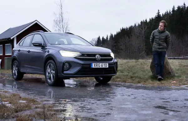 Grå VW Taigo står på en isig väg nära en röd stuga. En man står lutad mot en sten i bakgrunden.