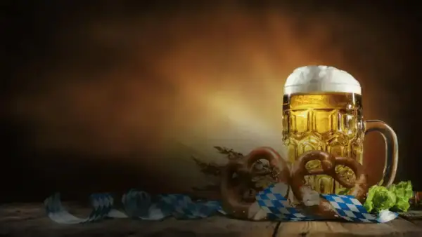 Boccale di birra dorata con schiuma abbondante, brezel e nastri a scacchi bianchi e blu, perfetti per le birre dell'Oktoberfest.