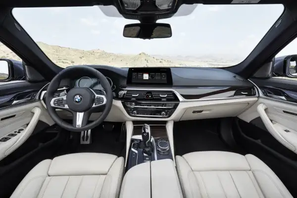 Wnętrze BMW 5 G30 z jasną tapicerką, drewnianymi wstawkami i nowoczesnym ekranem multimedialnym.