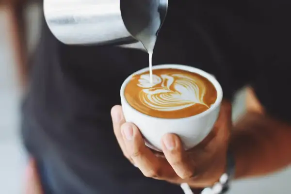 Un barista crea un disegno a latte art su un cappuccino. Latte versato nel caffè per un cappuccino prima latte o caffè perfetto.