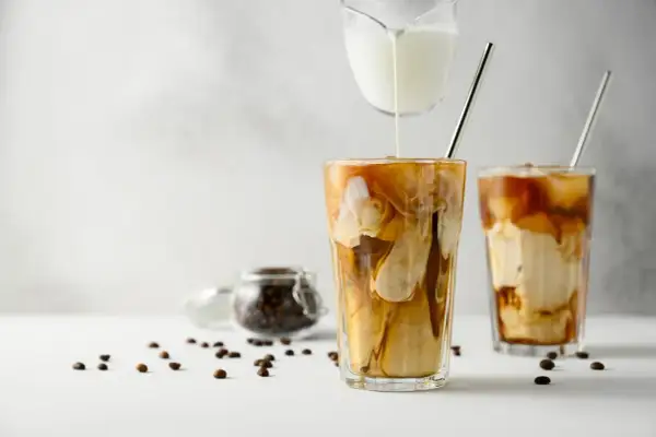 Versare latte freddo in un bicchiere di caffè ghiacciato crea un effetto marmorizzato invitante. Chicchi di caffè sparsi completano la scena.