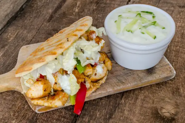 Gyros z kurczakiem, warzywami i sosem tzatziki na desce drewnianej.