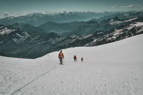 Trois alpinistes progressent sur un glacier enneigé, le Mont Rose en toile de fond. L'ascension est spectaculaire.