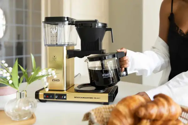 En gyllene Moccamaster brygger kaffe, perfekt för en italiensk frukost med nybakade croissanter.