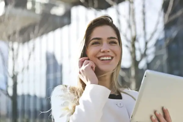 Donna sorridente con tablet, forse sta per uscire prima dal lavoro senza permesso, con un'aria di gioia e libertà.