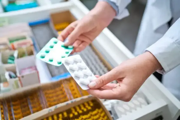 Farmaceuta wybiera leki z szuflady. W rękach trzyma opakowania z tabletkami, być może metotreksat, przygotowując je dla pacjenta.