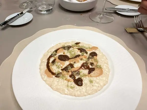 Un risotto cremoso con salse scure e chiare, guarnito con erbe verdi. Andrea la Rossa lo ha preparato con cura.