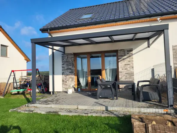 Nowoczesna pergola z poliwęglanowym dachem chroni taras z meblami. Idealne miejsce na relaks.