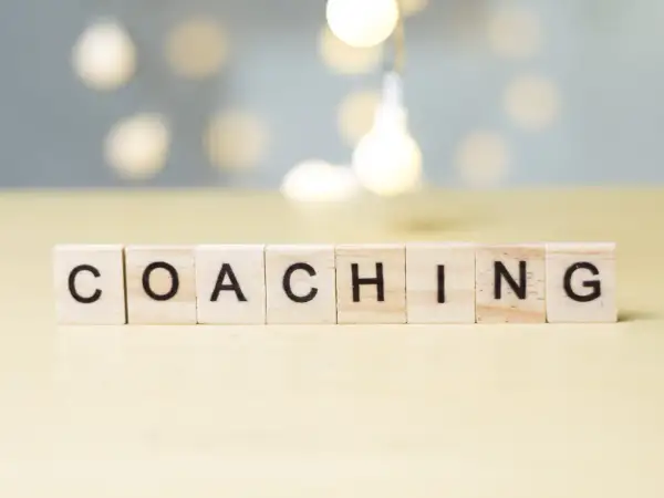 Drewniane klocki z literami układają słowo "COACHING". To właśnie kim jest coach – osoba wspierająca rozwój.