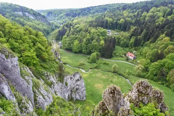 Malownicza dolina Prądnika z krętą rzeką, skalnymi ostańcami i domkami ukrytymi wśród zieleni.