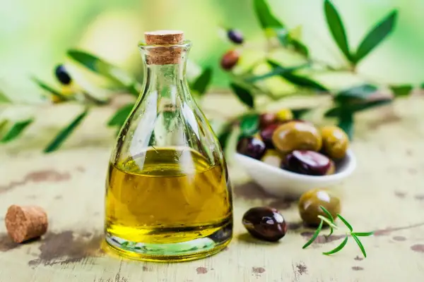 Olio di sansa in bottiglia di vetro, con olive miste e rametto di rosmarino. Un condimento versatile, l'olio di sansa è commestibile e perfetto per ogni piatto.
