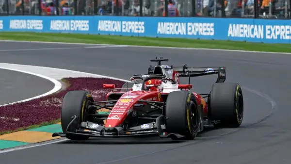 Un'auto di F1 in gara, con livrea rossa Ferrari, sfreccia in curva. La pubblicità "American Express" fa da sfondo a questa emozione da vedere in TV.