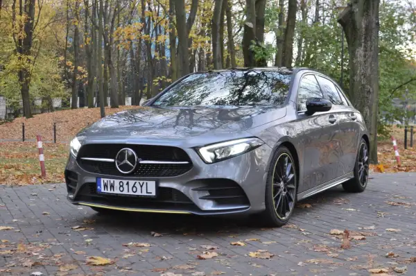 Szary hatchback Mercedes Klasa A zaparkowany na chodniku wśród jesiennych liści.