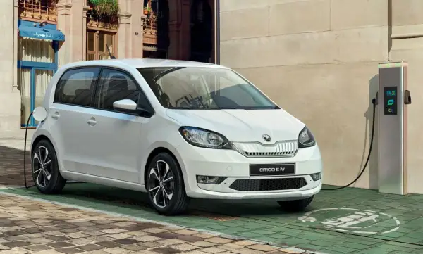 Biały Skoda Citigo e IV ładuje się przy stacji ładowania na brukowanej uliczce, gotowy na miejskie przygody.
