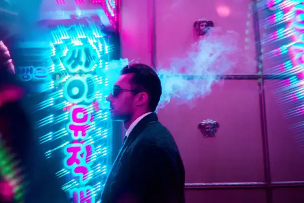 Man exhales smoke in front of vibrant neon signs, a cool example of led light photography ideas.