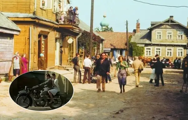 Scena z filmu "Znachor" kręcona w malowniczej wsi. W tle drewniane domy, a na pierwszym planie para na motocyklu.