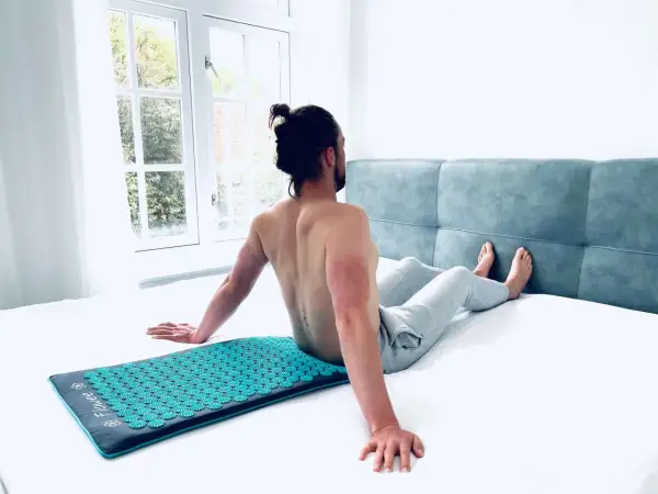 Man zit op een spijkermat, genietend van de ontspanning. De vraag is: hoe lang op spijkermat liggen voor optimaal effect?