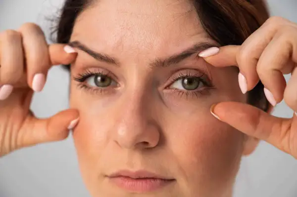 Dita che sollevano la pelle per mostrare come truccare gli occhi con palpebre cadenti, creando un effetto lifting.