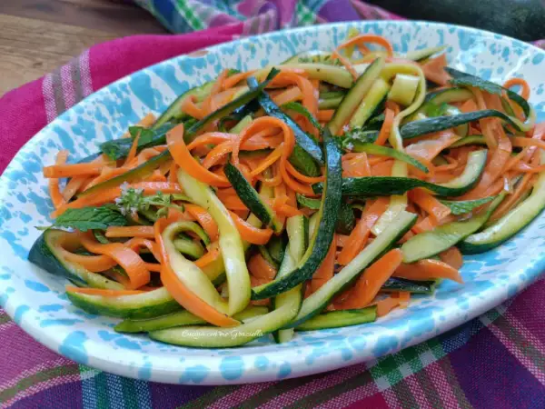 Deliziose zucchine alla julienne con carote, guarnite con menta fresca, servite su un piatto colorato.