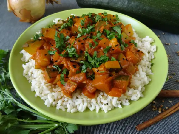 Pyszna cukinia w curry z ryżem, posypana świeżą natką pietruszki i czarnuszką. Aromatyczne danie, które zachwyci każdego.
