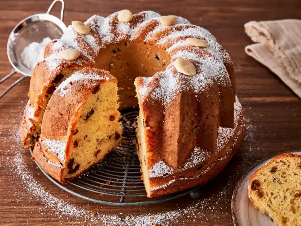 Ein köstlicher Gugelhupf-Kuchen mit Rosinen und Mandeln, bestäubt mit Puderzucker. Der Gugelhupf-Kuchen geht nicht aus der Form, aber ein Stück wurde bereits herausgeschnitten.