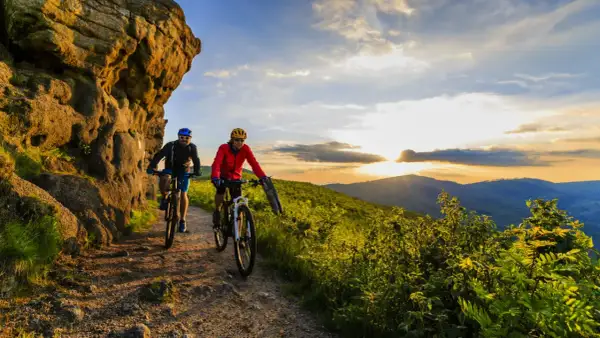 Dwóch rowerzystów przemierza malownicze trasy rowerowe w górach o zachodzie słońca.