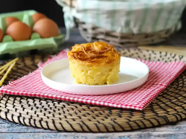 En gyllene, krispig makaronipudding på en vit tallrik, perfekt för ett maskros recept. Ägg i bakgrunden.