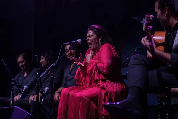 Una cantante colombiana flamenco, con un vestido rojo vibrante, canta apasionadamente acompañada por guitarristas.