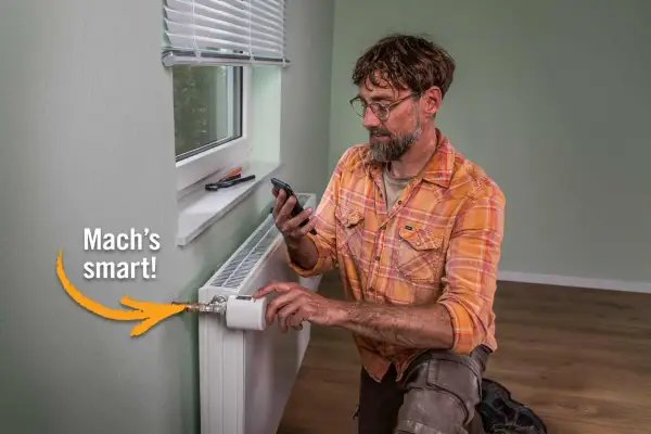Mann mit Smartphone installiert smarten Thermostat an Heizkörper. Einfach das Thermostat wechseln und Energie sparen.