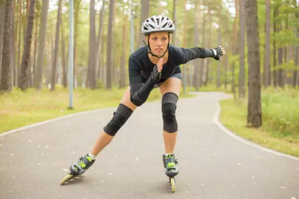 Kobieta w kasku i ochraniaczach jeździ na rolkach po leśnej ścieżce. Czy jazda na rolkach odchudza? Tak, to świetny trening!