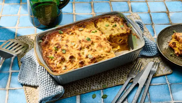 Herzhafte Moussaka mit Zucchini, goldbraun gebacken, wartet darauf, serviert zu werden. Ein Stück ist bereits auf einem Teller angerichtet.