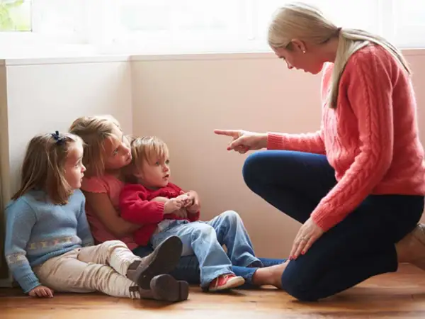 Kvinna pekar på barn som sitter på golvet. Kanske ett svårt samarbetssamtal med narcissist.