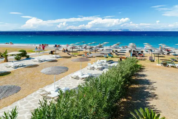 Słoneczna plaża Faliraki by Sun Palace z leżakami i parasolami. Turkusowe morze i góry w tle.