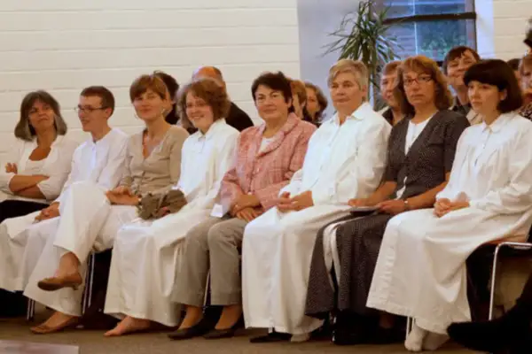 Frauen in weißen Gewändern sitzen nebeneinander. Die Kleidung könnte auf eine religiöse Gemeinschaft hindeuten, wo Baptisten Regeln für Frauen haben.