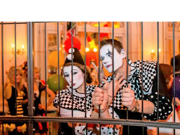 Zwei Clowns hinter Gittern, bereit für den Dresden Karneval. Bunte Ballons und Lichter im Hintergrund.